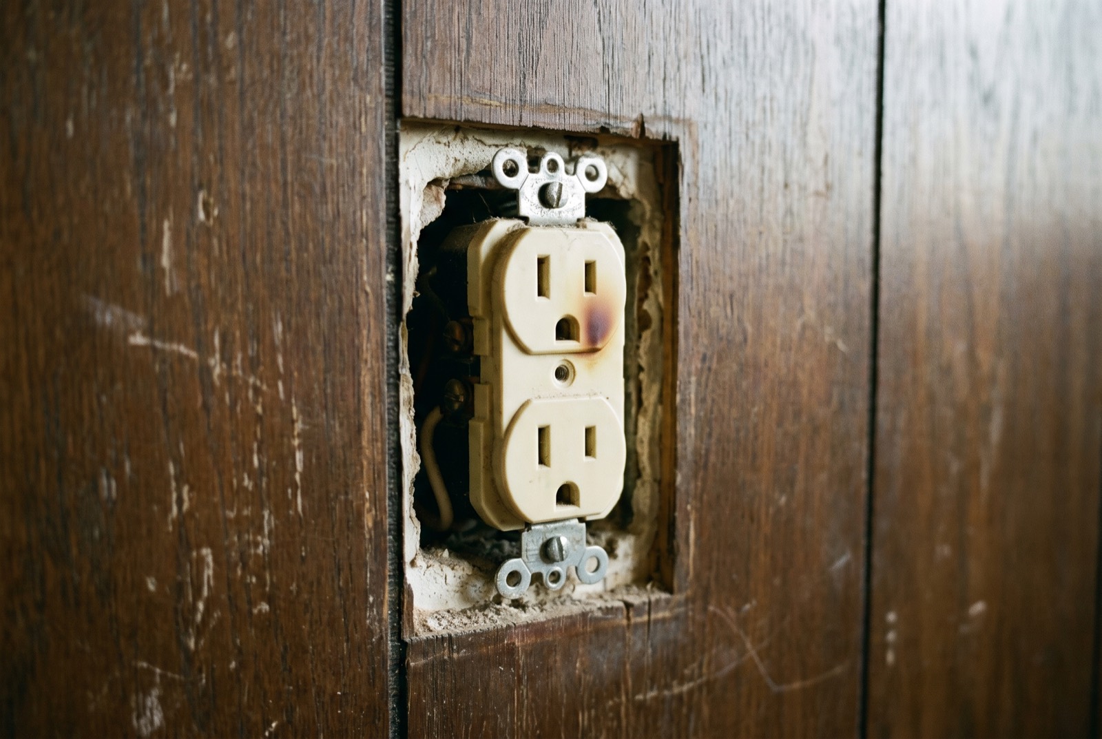 A wall outlet with its cover removed and a scorch mark near one slot